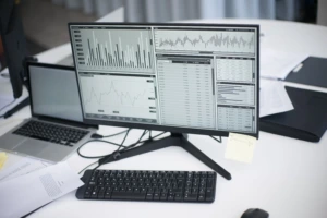 Kompiuterio monitoriuje rodomi finansiniai duomenys, grafikai ir rinkos rodiklių lentelės